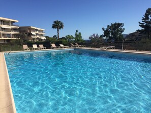 En klar, blå pool med liggestole og udsigt til en bygning i flere etager i baggrunden.