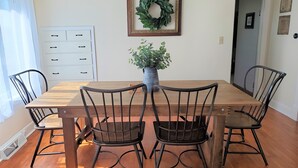 A dining room with a wooden table and four chairs, a potted plant, a white cabinet, and a framed wreath on the wall. - Charming Nauvoo Farmhouse - 1 mile from Nauvoo Temple (Nauvoo)