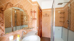 A bathroom with a large mirror, a sink with a marble countertop, and a glass-enclosed shower area. - S'Omu and Assunta 1P by All4sardinia  (Cardedu)
