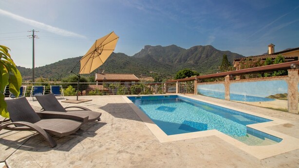 A swimming pool with lounge chairs, a sun umbrella, and a mountain view. - S'Omu and Assunta 1P by All4sardinia  (Cardedu)