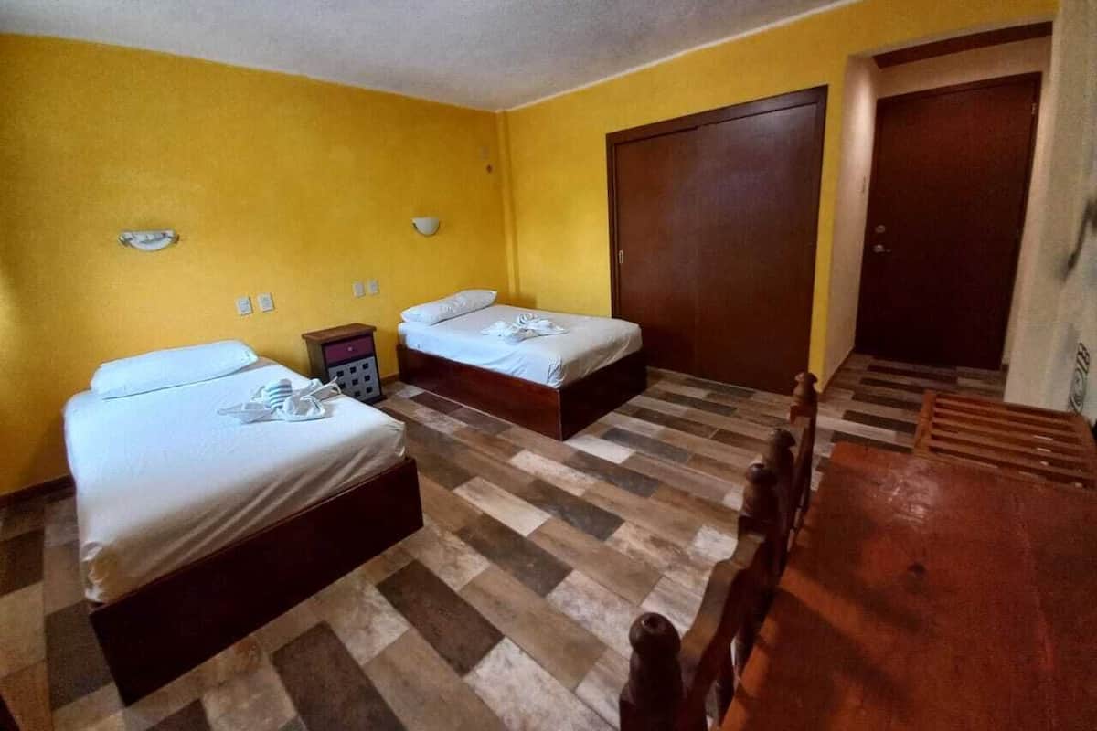 Una habitación de hotel con dos camas, una mesa de madera y un armario.