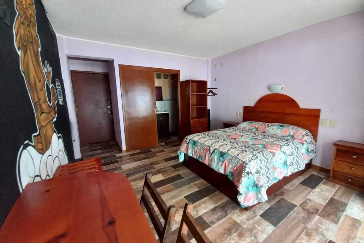 Un dormitorio con cama, muebles de madera, suelo de baldosas y una puerta que da a otra habitación.