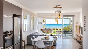 A modern kitchen with a large island, a dining area with a view, and a living space with a sofa and a TV. - Ayia Thekla Seafront Villa Dagi (Ayia Napa)