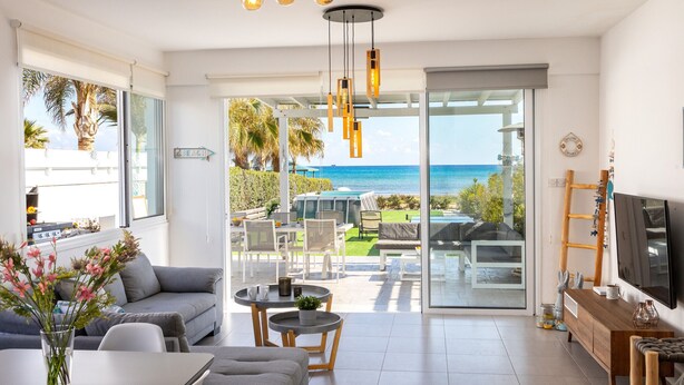 A modern living room with a large sliding glass door leading to a balcony with a view of the sea. - Ayia Thekla Seafront Villa Dagi (Ayia Napa)