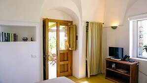 Ein Schlafzimmer mit Holztür, einem Fernseher auf einem Holzschrank, einem Bücherregal und einem Fenster mit Steinwand.