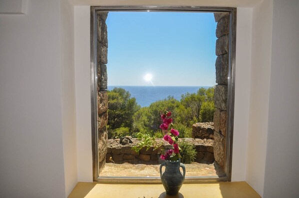 Une pièce avec vue sur la mer, encadrée par une fenêtre en pierre, et un vase rempli de fleurs posé sur une table.