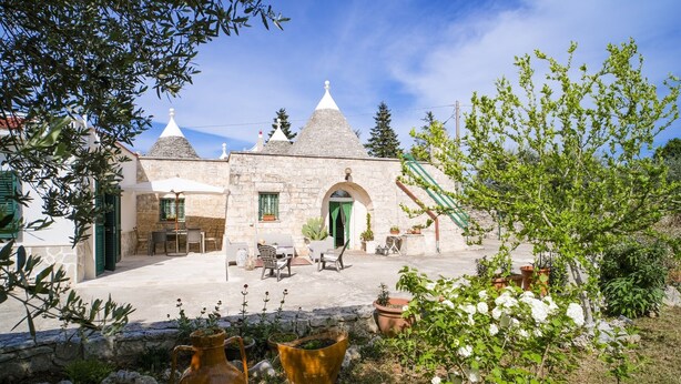 A stone building with a courtyard, outdoor seating, and potted plants. - Wonderful Trulli building in Locorotondo countryside (Locorotondo)