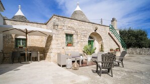 A stone building with a patio area featuring outdoor furniture, a table, and a staircase leading to an upper level. - Wonderful Trulli building in Locorotondo countryside (Locorotondo)