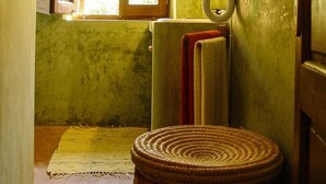 Une petite pièce peu éclairée, avec une seule fenêtre, un radiateur et un tabouret en osier.