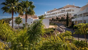 Un resort moderno con varias edificaciones blancas, palmeras y un jardín bien cuidado.