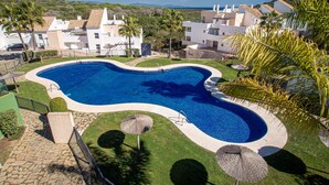 Una piscina rodeada de un césped cuidado, palmeras y vistas de edificios residenciales al fondo.