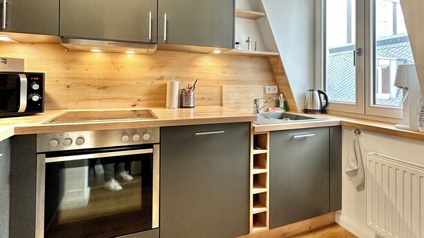 Eine moderne Küche mit grauen Schränken, einer Holzausziehtafel, einem eingebauten Ofen und einem Fenster mit Blick nach draußen.
