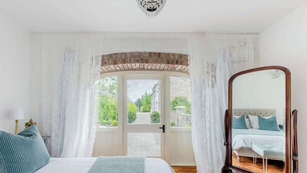 A bedroom with a large bed, a mirror, and a view of the outdoors through a door. - The Cow Shed—Luxury Barn Moments From Narberth (Narberth)
