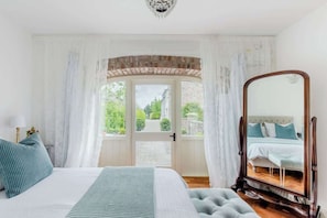 Een slaapkamer met een groot bed, een spiegel en uitzicht op de omgeving via een deur.
