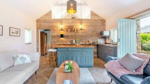 A cozy living room with a wooden ceiling, a blue kitchen island, and a stone wall. - The Cow Shed—Luxury Barn Moments From Narberth (Narberth)