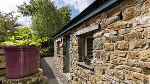 A stone building with a window and a door, surrounded by gravel and greenery. - The Cow Shed—Luxury Barn Moments From Narberth (Narberth)