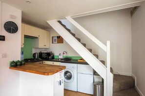 A compact kitchen with a washing machine, a wooden countertop, and a staircase leading to a loft bedroom.
