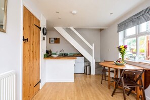 A modern kitchen with a wooden door, white cabinetry, a built-in stove, and a dining area with a table and chairs. - Cosy Bothy | Heart of Picturesque Solva Village (Solfach)