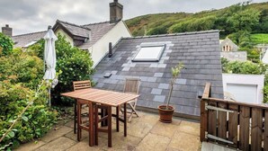 Eine Dachterrasse mit Holztisch und -stühlen, einem Blumentopf und Blick auf einen Hügelhang.