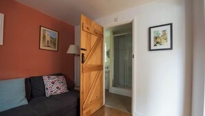 A room with a wooden door, a sofa with patterned cushions, and two framed pictures on the walls.
