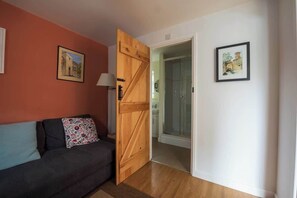 A room with a wooden door, a sofa with patterned cushions, and two framed pictures on the walls.
