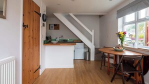 Eine Küche mit einer Holztür, einer weißen Treppe, einem Esstisch mit Stühlen und einem Fenster mit Blick.