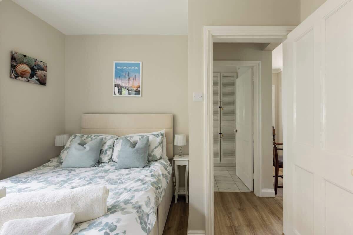 Une chambre à coucher avec un lit, des oreillers, une table de chevet, une affiche et une porte donnant sur une autre pièce.