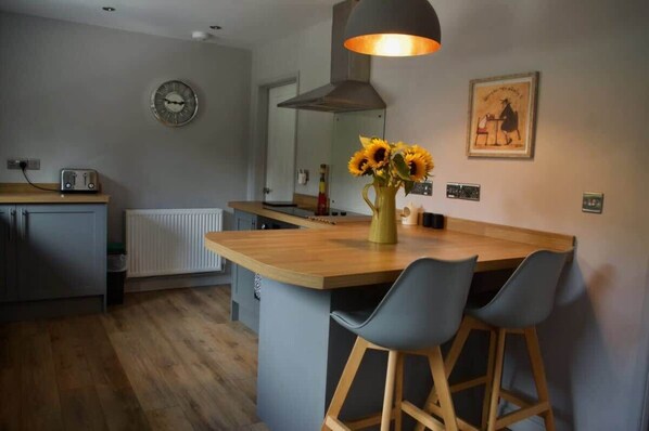 Una cocina moderna con una isla de madera, taburetes de bar, un reloj y un cuadro en la pared.
