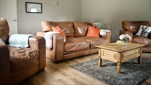 Ein Wohnzimmer mit einem braunen Ledersofa, einem Holztisch und einem grauen Teppich.