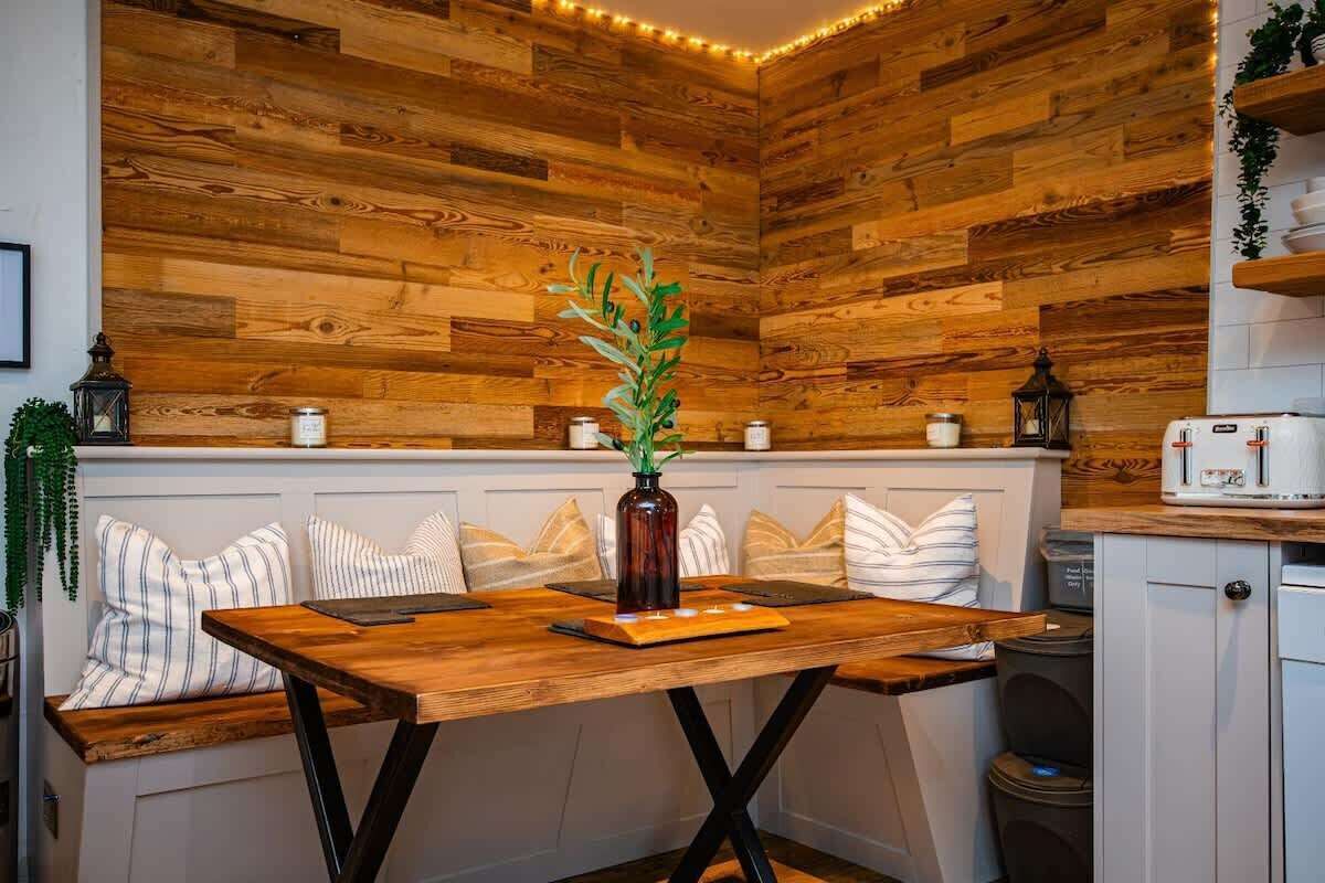 A cozy kitchen with a wooden wall, a wooden table, and a bench with striped cushions.