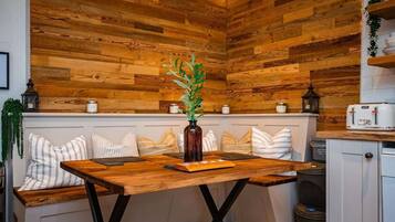 A cozy kitchen with a wooden wall, a wooden table, and a bench with striped cushions.