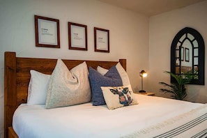 A neatly made bed with a wooden headboard, multiple pillows, and framed certificates on the wall.