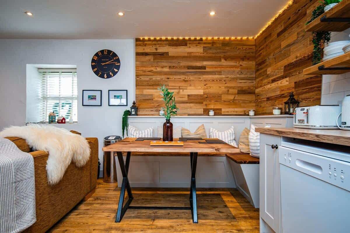 A cozy kitchen with a wooden wall, a clock, and a dining area with a table and chairs.