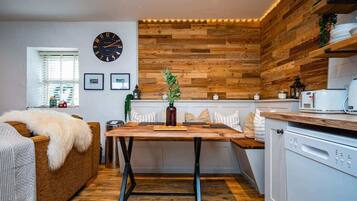 A cozy kitchen with a wooden wall, a clock, and a dining area with a table and chairs.