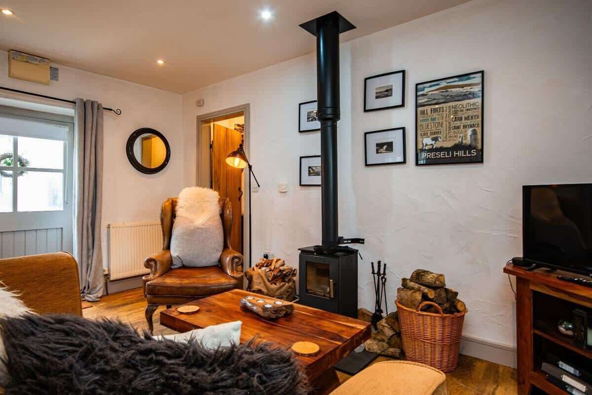 A cozy living room with a fireplace, a comfortable armchair, a television, and a bookshelf.