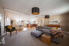 A spacious living area with a grey sofa, ottoman, and a wooden coffee table. A dining table and chairs are visible in the background.