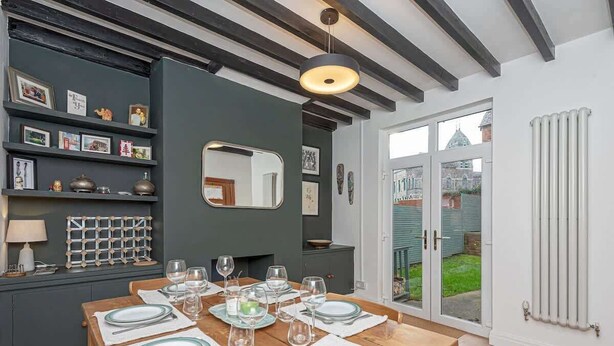 A dining area with a wooden table set for six, a dark wall with shelves, and a large mirror.