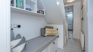 A modern, compact living space with a built-in bench, a white shelving unit with books, and a staircase leading to another level.