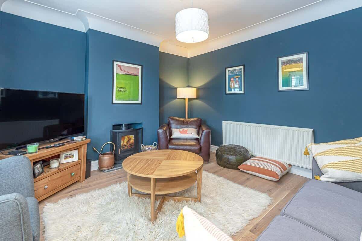 A cozy living room with a flat-screen TV, a wooden coffee table, a leather armchair, and a fireplace.