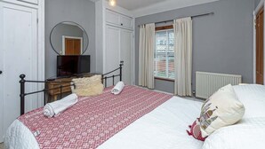 A bedroom with a bed, a mirror, a dresser, a television, and a window with curtains.