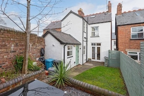 A residential property with a white exterior, a brick wall, and a small garden area with a lawn and a tree.