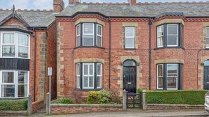 A red brick terraced house with a bay window, a front door, and a small garden area.