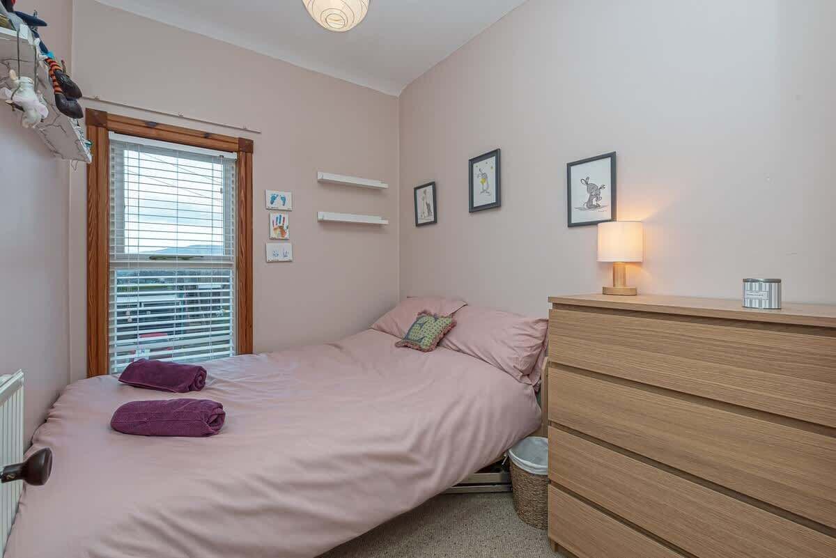 Un dormitorio con cama, cómoda, lámpara y ventana con persianas.