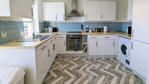 Una cocina compacta con armarios blancos, horno integrado, lavadora y suelo con un patrón de espiga.