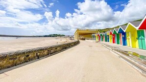 Una playa con una fila de coloridas cabañas playeras y un muro de piedra al frente.