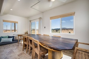 A spacious dining area with a large wooden table and chairs, large windows offering a view of the desert landscape, and a built-in bench along the wall.