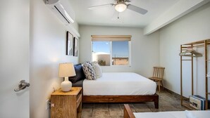 A bedroom with a bed, a ceiling fan, a window with a view, and a wooden cabinet.