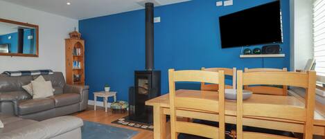 A living room with a blue wall, a fireplace, a television, and a dining area with wooden chairs and a table.
