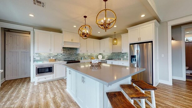 A modern kitchen with white cabinetry, a large island, and a stainless steel refrigerator.