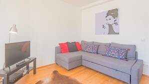 A living room with a grey sectional sofa, a flat-screen TV on a stand, a lamp, and a rug. - Melro's Places (Setúbal)